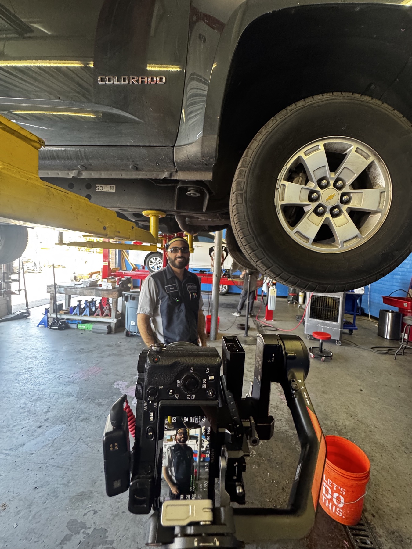 A Stray camera filming an automotive technician beneath a vehicle lift